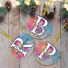 three round stickers with the letter r and p on them, sitting next to pine cones