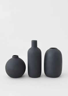 three black vases sitting next to each other on a white surface with no one around them