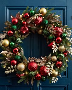 a christmas wreath on a blue door with red, green and gold ornaments hanging from it