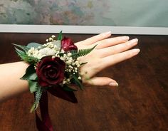 a woman's hand holding a red rose and white flower bouquet on her wrist