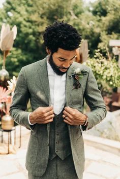 a man wearing a suit and tie standing in front of some flowers with his hands on his chest