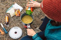 a person sitting on the ground next to food and camping gear, with a can of soda