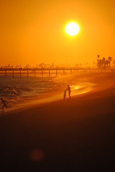 two people are playing on the beach at sunset