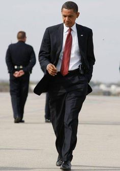 two men in suits are walking on the tarmac, one is wearing a red tie