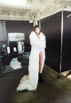 a woman in a white fur coat standing next to a black backdrop and some lights