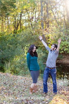 a man and woman standing next to each other in the woods with their arms up