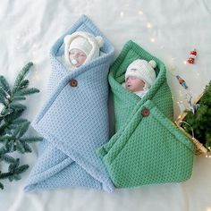 two babies wrapped up in blankets next to a christmas tree and small pine tree with lights