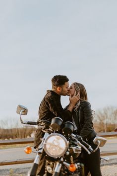 a man and woman kissing on the back of a motorcycle