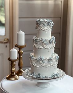 a three tiered cake sitting on top of a white table next to two candles