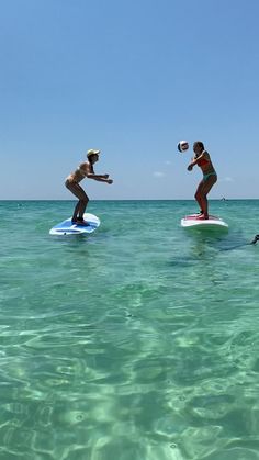 two people on surfboards in the ocean playing with a frisbee and ball