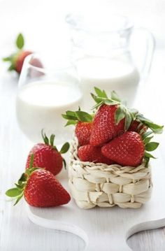 strawberries in a wicker basket next to a glass of milk on a white table