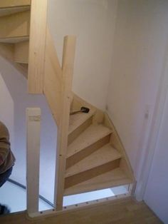 a man kneeling down in front of a wooden stair case next to a white wall