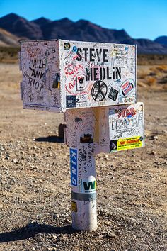 a street sign covered in stickers on the side of a dirt road