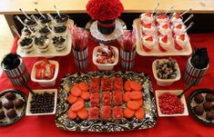 a table topped with lots of food and desserts on top of red cloth covered tables