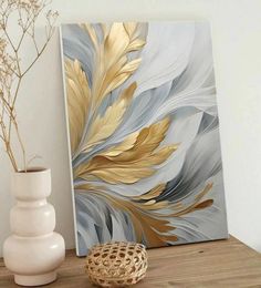 a white vase sitting on top of a wooden table next to a painting with gold leaves