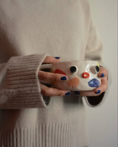 a woman is holding a cup with painted dots on it and her hands are wrapped around the mug