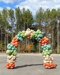 an arch made out of balloons sitting in the middle of a parking lot next to trees