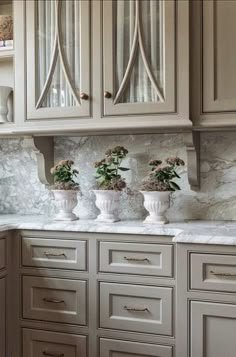 three white vases with flowers in them on a marble counter top next to cabinets