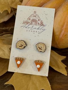 two pieces of wood are sitting on a card next to some leaves and pumpkins