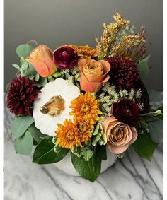 a white vase filled with lots of flowers on top of a marble countertop covered in greenery