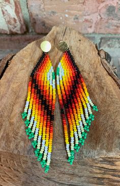 a pair of multicolored beaded earrings sitting on top of a piece of wood