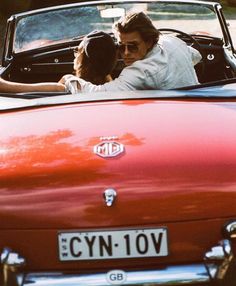 two people in an old red convertible car