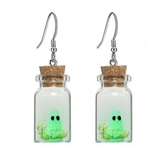 a pair of earrings with a green face in a glass jar