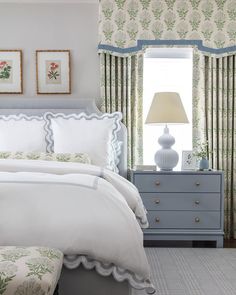 a white bed sitting in a bedroom next to a window covered in green and white curtains