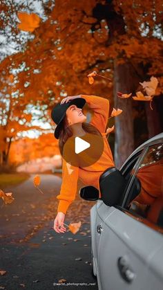 a woman in an orange sweater leaning out the window of a car with leaves flying around her