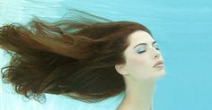 a woman floating in the water with her hair flying through the air above her head