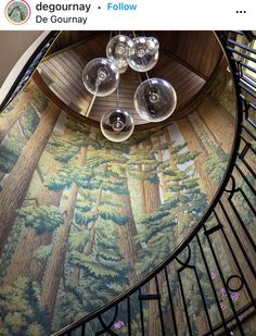 there are wine glasses sitting on the top of this spiral stair case with trees painted on it