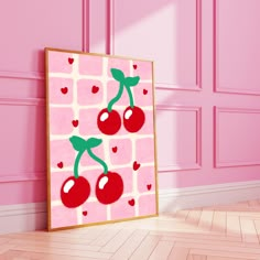 a painting on the wall with two cherries hanging from it's sides, in front of a pink background