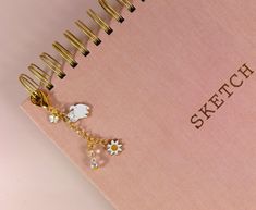 a pink notebook with a gold chain attached to it and charms hanging from the cover