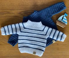 a blue and white knitted sweater next to a toy boat on a wooden table