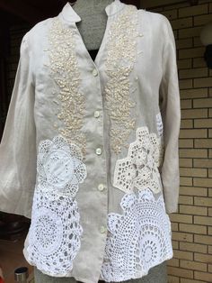 a mannequin wearing a white jacket with crocheted laces and flowers