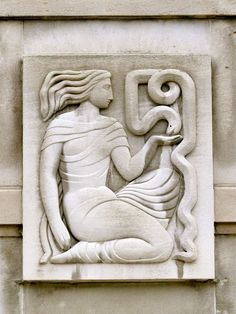 a statue on the side of a building with a woman holding a snake in her hand