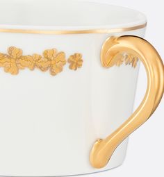 a white and gold coffee cup with flowers on the side, decorated with golden leaves