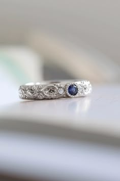 a white gold wedding band with two blue sapphires on top and an intricate filigree design in the middle