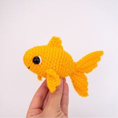 a hand holding a small yellow crocheted goldfish