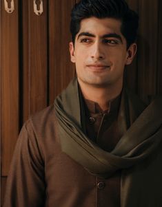 a man wearing a brown shirt and green scarf standing in front of wooden closets