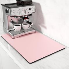 a pink placemat with two coffee cups on it next to an espresso machine