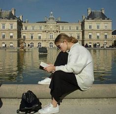 a woman sitting on the edge of a fountain looking at her cell phone and reading