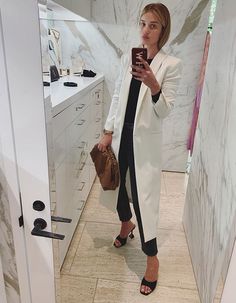 a woman taking a selfie in a bathroom mirror while holding a purse and looking at her cell phone