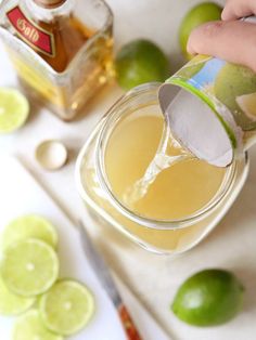 a person pours an alcoholic drink into a glass with lime slices around the rim