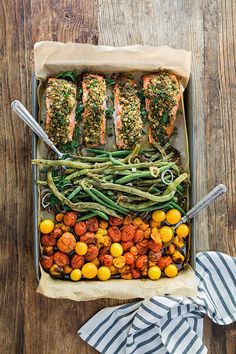 salmon, green beans and tomatoes in a baking dish on a wooden table with striped napkins