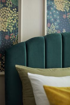 a green headboard with yellow and white pillows on top of it next to wallpaper