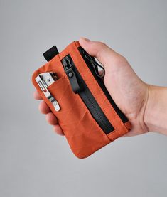 a hand holding an orange wallet with two keys in it and a cell phone inside