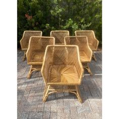 four wicker chairs sitting on top of a brick floor next to some green trees