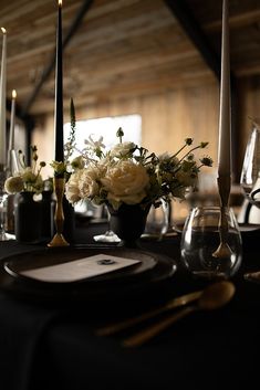 a table set with candles and flowers in vases on top of black cloth covered place settings