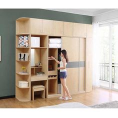 a woman standing in front of a wooden closet with drawers and shelves on the wall